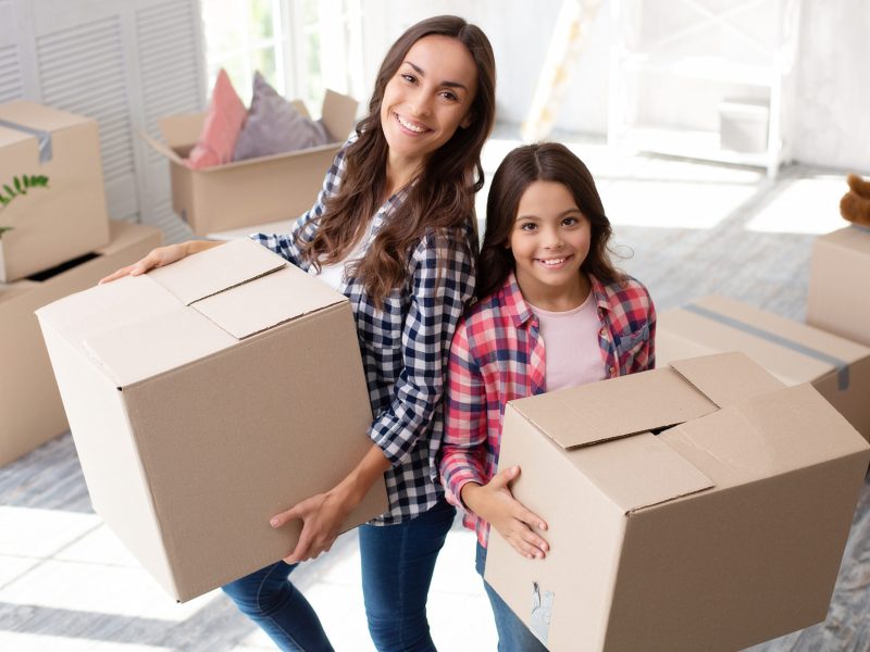 Alluring young woman and her child are holding cardboard boxes in their new house after the relocation.